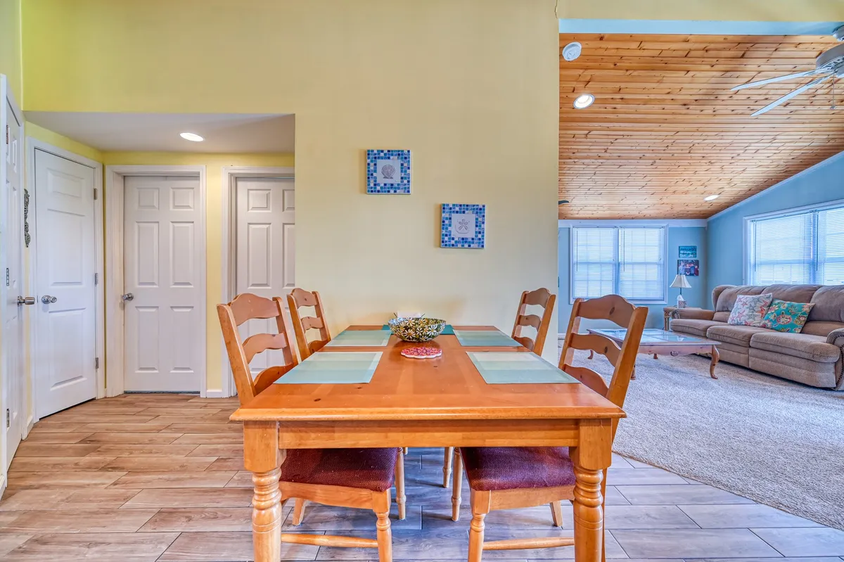A welcoming dining and living space featuring a wooden dining table, colorful wall art, and a comfortable sofa. The room exudes a cozy, communal ambiance perfect for friendly gatherings and shared meals. The space is bright, inviting, and designed for group interaction, with the table set up for social events or game nights.