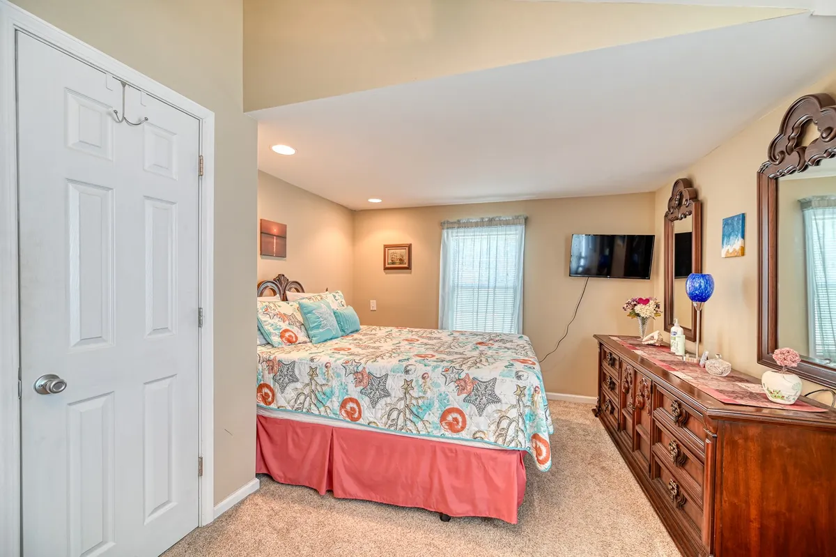 A serene bedroom scene with a bed featuring colorful bedding, a wooden dresser adorned with decorative items, and mirrors that reflect natural light throughout the room. The atmosphere is calm, comfortable, and ideal for winding down after a day of local adventures.