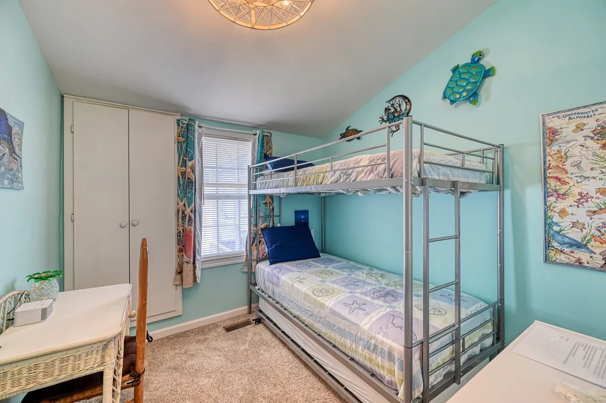 A playful bunkroom featuring a twin-over-twin bunk bed, trundle, colorful wall decor, and a small desk. The space feels cheerful and welcoming, designed for kids or friends to sleep, play, or study.