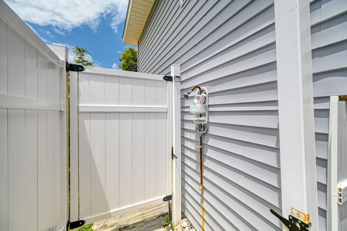 A quiet side yard bordered by a white fence and shaded by nearby greenery. The peaceful, private atmosphere is ideal for letting pets stretch their legs or for owners to enjoy a tranquil outdoor moment together.