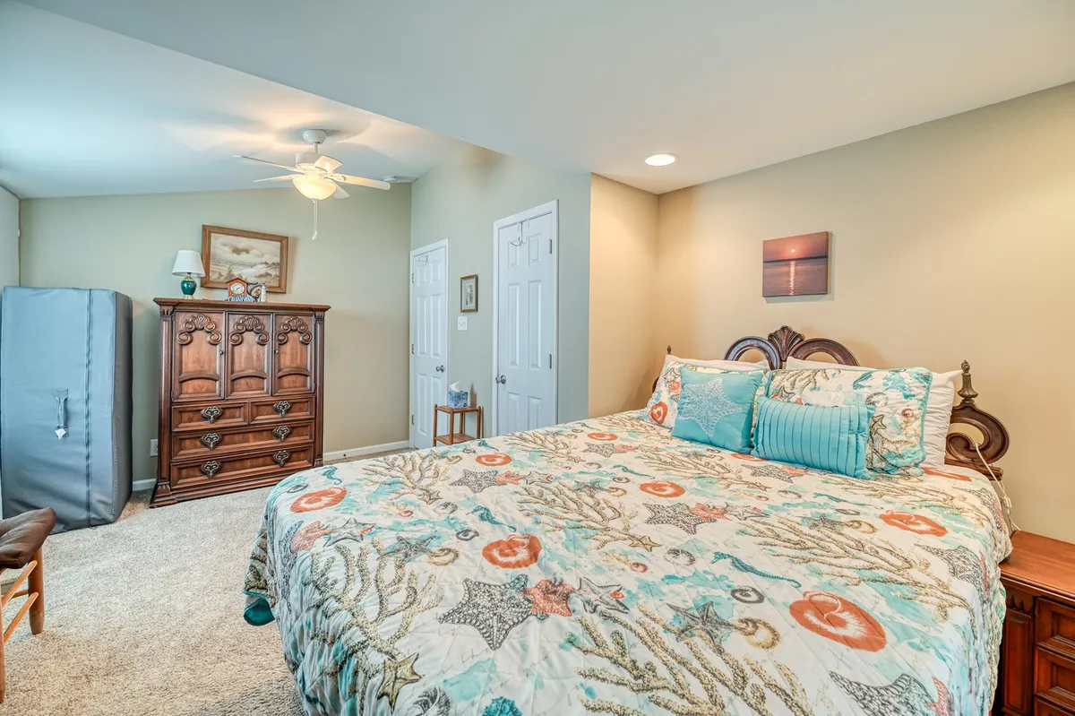 A cozy bedroom with a bed dressed in colorful bedding, a wooden dresser, and decorative artwork on the walls. Sunlight filters through the window, creating a warm and inviting space perfect for rest and relaxation.
