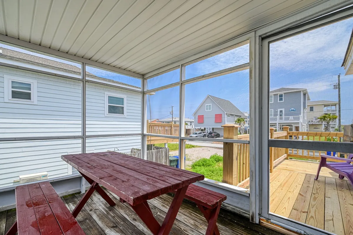 A casual, family-friendly interior with a wooden picnic table, large windows, and abundant natural light. The windows reveal a view of the outdoors, and the setup hints at a space used for meals, games, and relaxed get-togethers.
