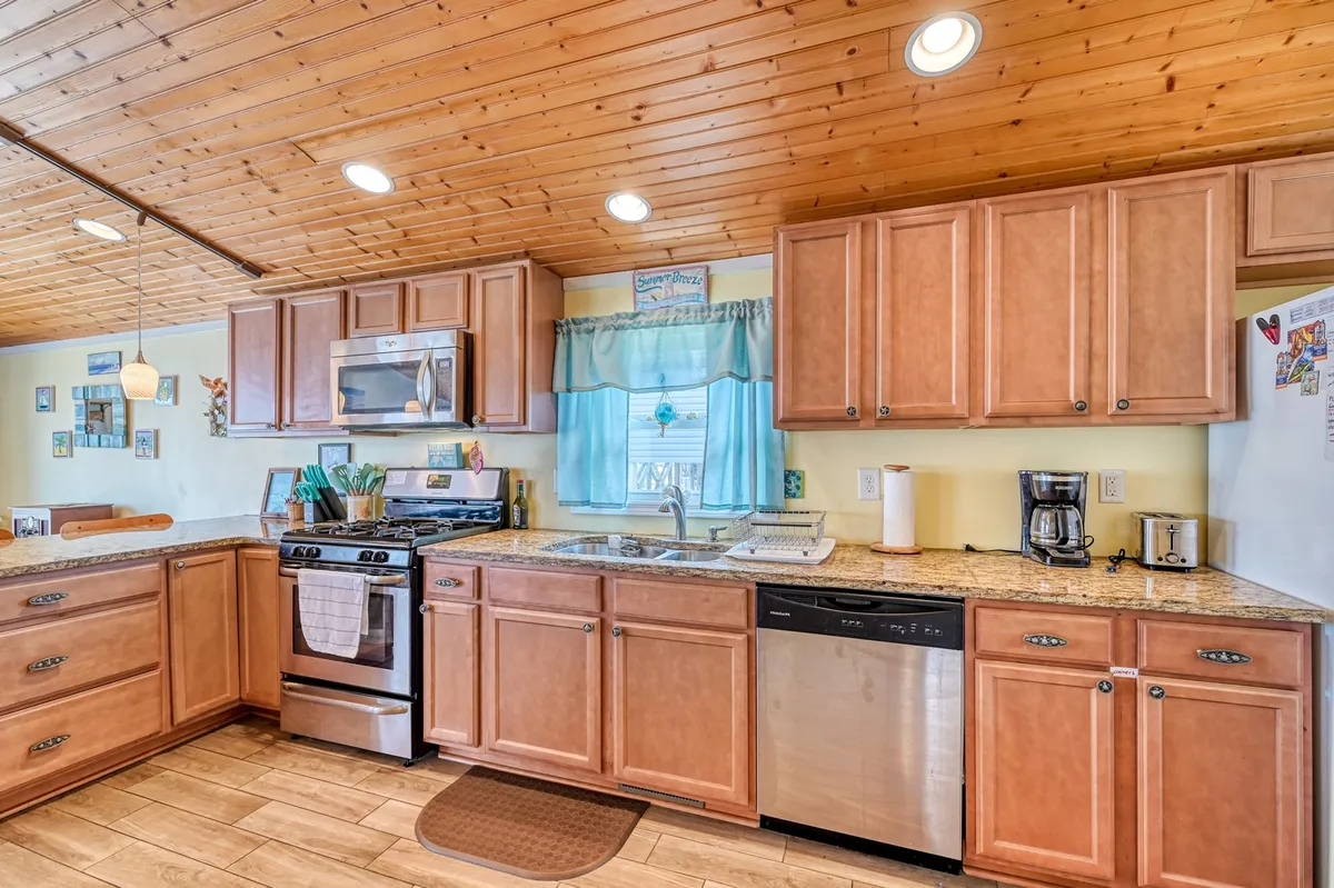 A cozy kitchen view highlighting granite countertops, sleek stainless steel appliances, a warm wooden ceiling, and blue curtains that add a pop of color. The space feels inviting and functional, ready for family cooking and casual breakfasts at the counter.