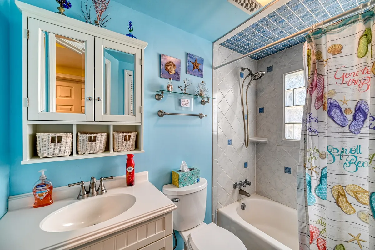 A bright bathroom with a colorful shower curtain, storage vanity, and decorative shell artwork. The space is clean, playful, and functional—ideal for quick morning routines or unwinding after beach adventures.