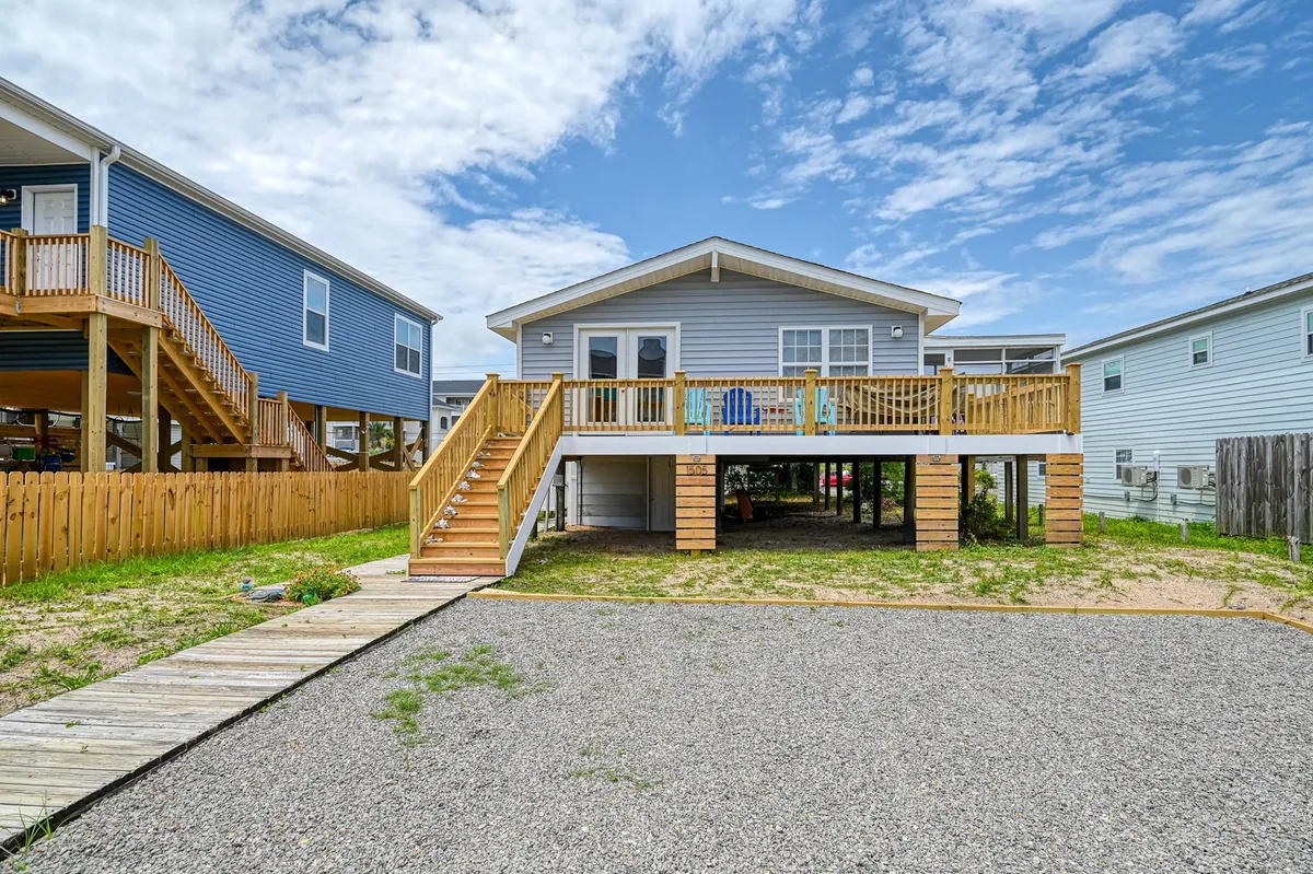A spacious deck with blue chairs and stairs leading down, surrounded by neighboring homes. The setting suggests a spot for morning coffee or watching sunsets, and the open space is ideal for family gatherings and barbecues.